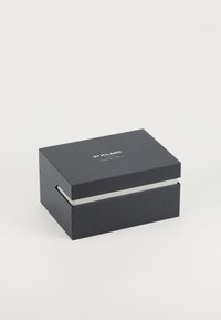 Scatola rettangolare nera con superficie texturizzata, con un interno bianco e un logo sul coperchio. Design minimalista con linee nette.