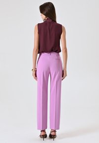 Bordeaux mouwloze blouse gecombineerd met hoogtaille lavendel wijde broek, wat zorgt voor een gladde textuur en een op maat gemaakte pasvorm. Bronzen hakken maken de look compleet.