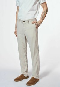 Jasnobeżowe, lniane spodnie o prostym kroju, z bocznymi kieszeniami i zapięciem na guzik. W zestawie brązowe zamszowe buty wsuwane.