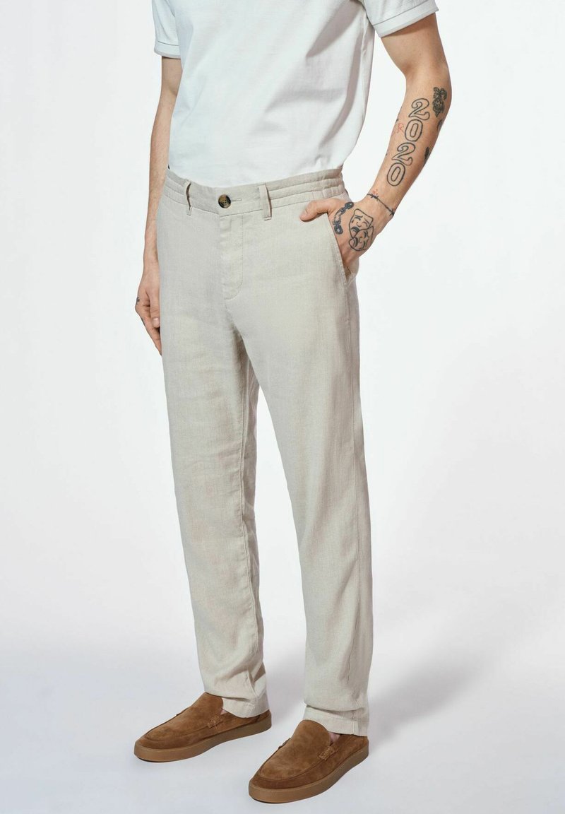 Jasnobeżowe, lniane spodnie o prostym kroju, z bocznymi kieszeniami i zapięciem na guzik. W zestawie brązowe zamszowe buty wsuwane.