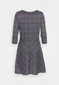 Robe à motifs checkés noir et blanc avec des manches trois-quarts, un corsage ajusté, une jupe évasée et un col rond. Le dos est fermé par un zip.