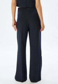 Mörkblå vida byxor med en slät textur, med hög midja och sidsömmar. Bakifrån visar de en skräddarsydd passform med vertikala veck.