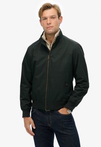 Chaqueta bomber verde oscuro con cremallera frontal, puños y cuello de canalé. Cuenta con bolsillos laterales y una tela suave y resistente al agua.