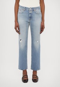 Jean droit bleu clair en denim, avec des détails usés et des ourlets effilochés, associé à des chaussures noires.