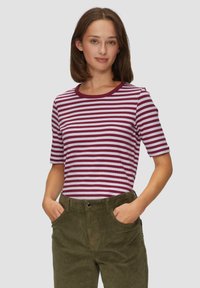 Czerwono-biała w paski koszulka z krótkim rękawem i okrągłym dekoltem, w połączeniu z zielonymi spodniami z sztruksu. Prosty, codzienny fason.