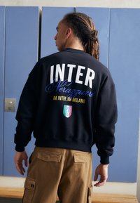 Crna dukserica s natpisom "INTER" u velikom bijelom tekstu i "Nerazzurri" u plavoj kurzivnoj fontu, s logotipom i brojem "20" na dnu.