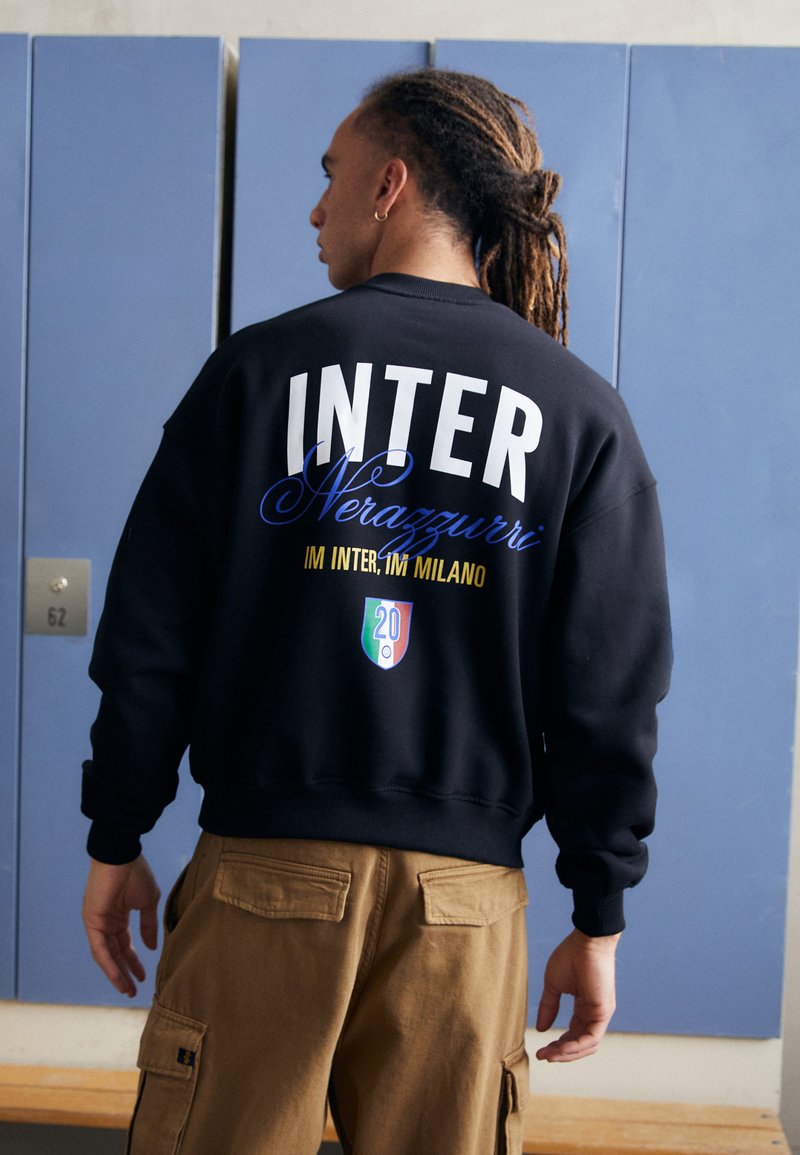 Crna dukserica s natpisom "INTER" u velikom bijelom tekstu i "Nerazzurri" u plavoj kurzivnoj fontu, s logotipom i brojem "20" na dnu.