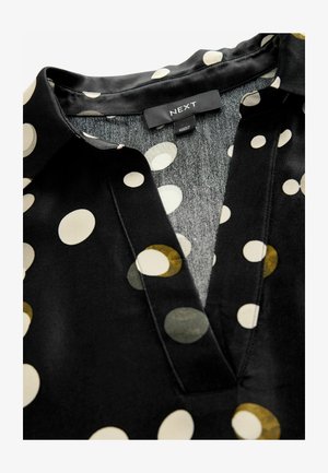 Schwarze Bluse mit großen cremefarbenen, grünen und senfgelben Kreisen. Weicher Stoff mit Kragen und einem dezenten V-Ausschnitt. Markenschild sichtbar.