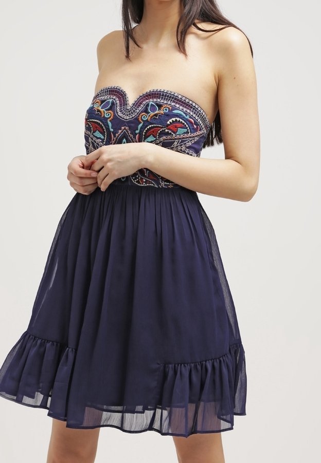 Robe bleu marine bustier brodée de couleurs, taille cintrée et jupe fluide avec ourlet volanté portée par une femme.