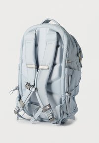 Ανοιχτό μπλε επενδεδυμένο σακίδιο ορειβασίας με ρυθμιζόμενους ιμάντες, πλαϊνές τσέπες και το λογότυπο The North Face στον ιμάντα, απεικονισμένο από πίσω σε λευκό φόντο.