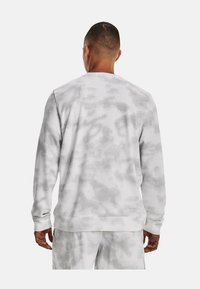 Hombre de espaldas, vistiendo un sudadera de color gris claro y blanco con un diseño de tie-dye, junto con pantalones a juego, frente a un fondo liso.