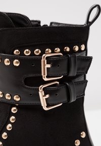 Tige de botte noire avec deux boucles dorées et des clous dorés décorant les lanières en cuir et le matériau en suède.