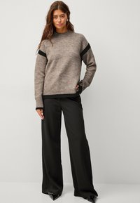 Maglione marrone a maglia con dettagli neri, scollatura rotonda e polsini a coste, abbinato a pantaloni neri a vita alta e gamba ampia, con scarpe a punta.