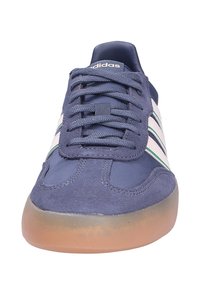 Navy blue Adidas sneaker with white and green side stripes, textured laces, suede details, and a translucent gum sole, shown from front view.