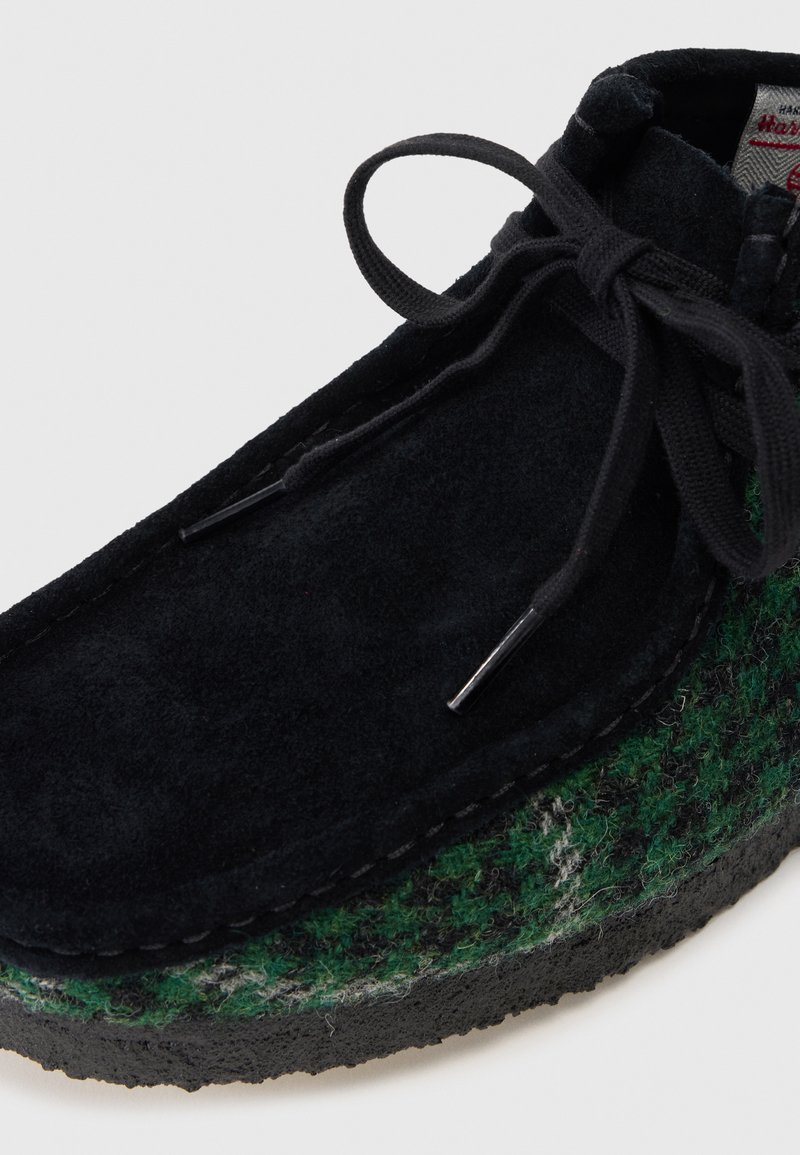 Black suede ankle shoe with green and gray patterned wool trim, textured rubber sole, and black laces secured with metal aglets.
