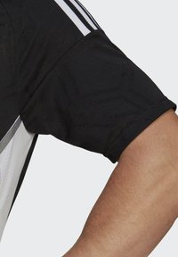 Black athletic shirt with short sleeves, featuring a textured geometric pattern and contrasting white stripes along the shoulder seam.