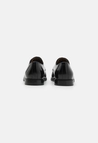 Chaussures habillées en cuir noir avec une finition lisse, à bout arrondi et à talon bas. Design minimaliste avec des détails de couture subtils sur les côtés.