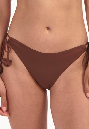 Mutandine bikini marroni con lacci laterali indossate da una persona che mostra la zona addominale e la parte superiore delle cosce su uno sfondo bianco.