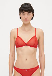 Rdeč prosojen mrežasti bralet z trikotnimi košaricami, nastavljivimi naramnicami, čipkastim okrasom in majhnim kamnom na sredini.