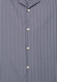 Chemise à boutons avec de fines rayures verticales blanches sur un tissu gris, dotée d’un col et de quatre boutons blancs visibles.