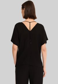 Czarny top z krótkim rękawem, z dekoltem w kształcie V z tyłu, z detalem w postaci sznureczka przy szyi oraz fakturowanym wykończeniem po bokach.