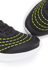 Black athletic shoes with circular yellow stitching, textured mesh upper, and white rubber soles, featuring a sleek design and low profile.