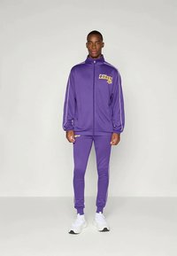 Trening violet fabricat dintr-un material neted. Geacă cu fermoar cu dungi albe și logo-ul "Lakers". Pantaloni ajustați cu un design aerodinamic.