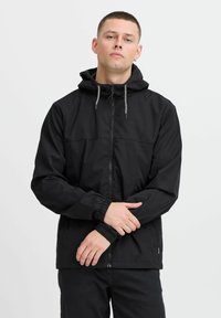 Jachetă neagră cu fermoar, cu glugă, manșete elastice și șnur. Material neted, design simplu și închidere frontală cu fermoar.