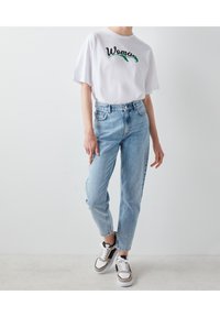 Valkoinen t-paita, jossa on vihreällä ja mustalla brodeerattu "Woman", yhdistettynä vaaleansinisiin korkeavyötäröisiin farkkuihin sekä harmaisiin, mustiin ja valkoisiin lenkkareihin.