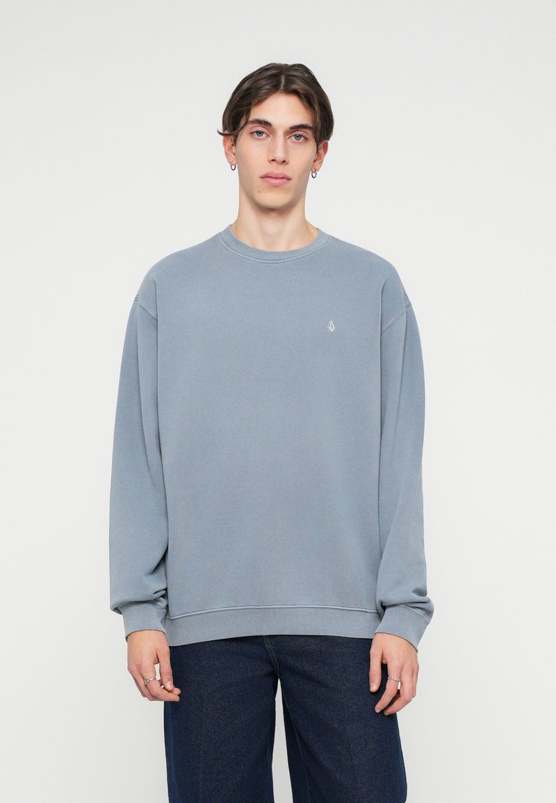 Szary sweatshirt wykonany z miękkiej bawełny, z okrągłym dekoltem i opadłymi szwami na ramionach. Posiada małe logo na piersi oraz ściągacze na rękawach.