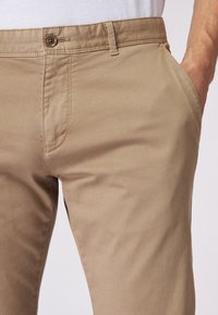 Pantalones de algodón beige con corte recto, bolsillos frontales y cierre de botón en la cintura. Textura suave con mínimos detalles de costura.