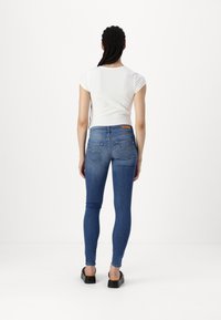 Cienkie niebieskie dżinsy wykonane z denimu, z średnim stanem, tylnymi kieszeniami z detalami przeszyć oraz metką na pasku.