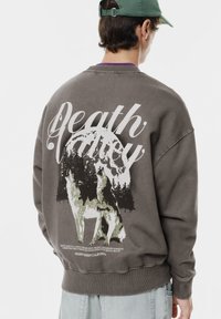 Szürke kapucnis pulóver, amelyen egy nagy grafikán farkas és fák láthatók, a hátoldalon pedig kiemelten szerepel a "Death Valley" felirat.