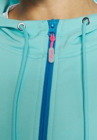 Sudadera con capucha de cremallera en azul claro, con cremallera azul contrastante y tirador rosa. Cuenta con cordones en la capucha y ojales en color plata.