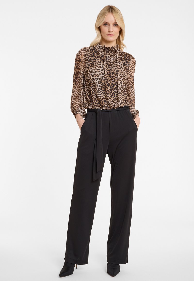 Woman wearing a high-neck leopard print blouse with long sleeves tucked into high-waisted black wide-leg trousers with a waist tie.