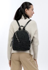 Svart ryggsäck av konstläder med blixtlåsfack, texturerad yta, dubbla remmar och ett litet övre handtag. Silverfärgade metallbeslag.