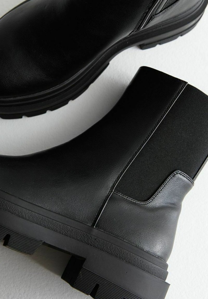 Bottines noires en cuir avec des panneaux en tissu extensible, semelles texturées et talons épais. Fini lisse avec des détails de couture minimalistes.