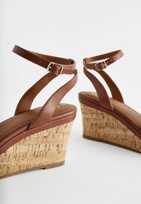 Sandali con zeppa in pelle marrone, caratterizzati da un tacco con texture in sughero, cinturini regolabili alla caviglia e una soletta liscia.