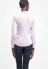 Langarmshirt in lichtroze en witte strepen, met een klassieke kraag, knoopmanchetten en een getailleerde pasvorm, gecombineerd met donkere spijkerbroek.