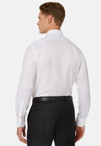 Camicia bianca a maniche lunghe con colletto classico, dotata di polsini con bottoni, indossata con pantaloni neri e una cintura in pelle nera.
