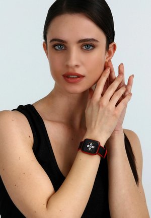 Smartwatch con quadrante quadrato nero, dettagli rossi e cinturino in silicone nero. Il display mostra quattro quadranti circolari. Design pulito, hardware minimale.