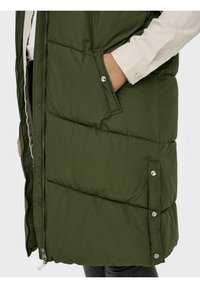 Chaleco acolchado verde con cierre de cremallera, bolsillos laterales y detalles de broche. Presenta un diseño acolchado y una textura elegante.