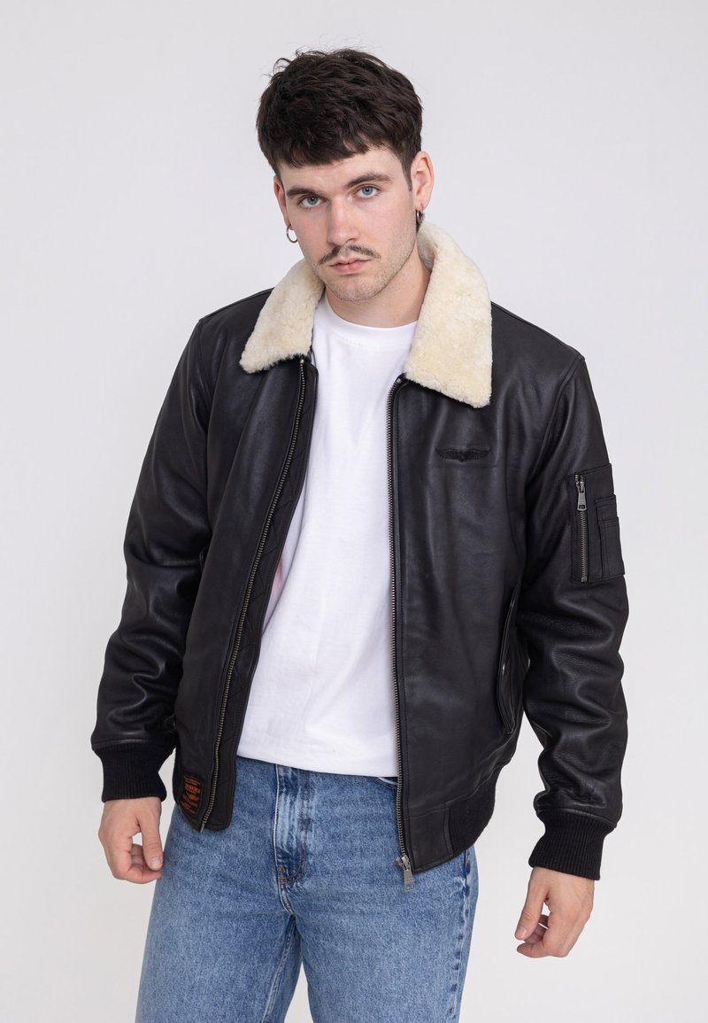Zwarte leren bomberjack met een crèmekleurige schapenvacht kraag, ritssluiting, geribbelde manchetten en een zijzak op de linkerarm.