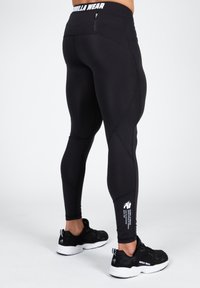 Black athletic leggings with a high waistband, seam detailing, and a small logo on the lower leg. Paired with black athletic shoes.