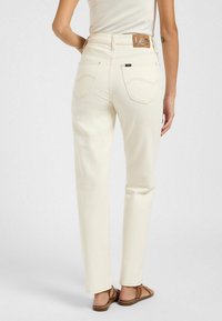 Jean droits de couleur crème avec des coutures contrastantes et un patch en cuir à l'arrière. Comprend deux poches arrière.