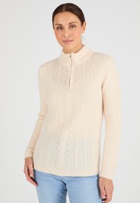 Suéter de punto beige claro con cuello alto y media cremallera, con patrones texturizados y mangas largas. Material suave y acogedor, ajuste casual.