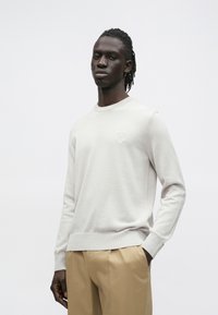 Svetlosivý sveter s okrúhlym výstrihom, rebrovanými manžetami a lemom. Na hrudi má malú textúrovanú značku, vyrobený z mäkkej látky.