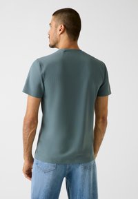 Herren-Kurzarmhemd in gedämpftem Türkis, aus glattem, leichtem Stoff mit Rundhalsausschnitt und legerer Passform.