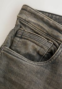 Gros plan d'un jean en denim noir délavé montrant une poche avant et une petite poche à monnaie avec des coutures et des rivets visibles.