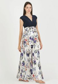 Robe de maternité avec un haut bleu marine et une jupe évasée en blanc, ornée de fleurs violettes, roses et bleues, avec un détail de nouage à l'avant.